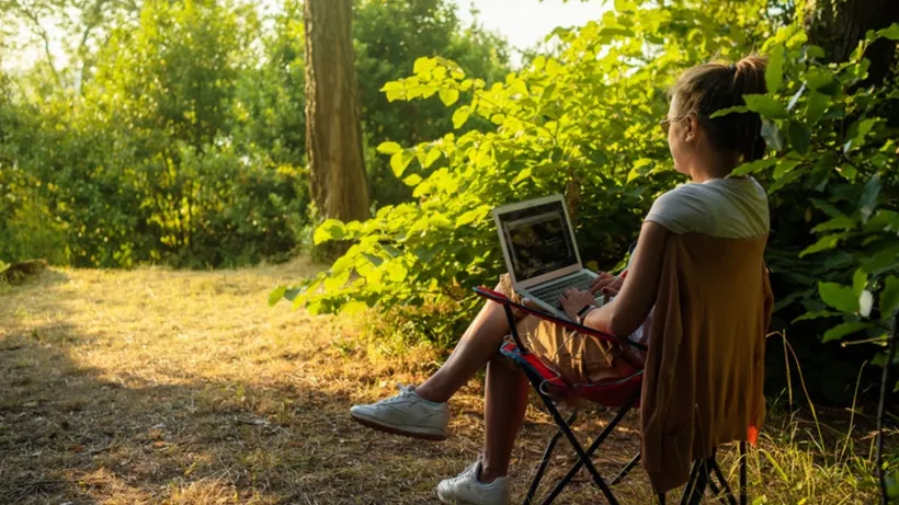 Frau arbeitet entspannt mit Laptop im Grünen bei warmem Abendlicht